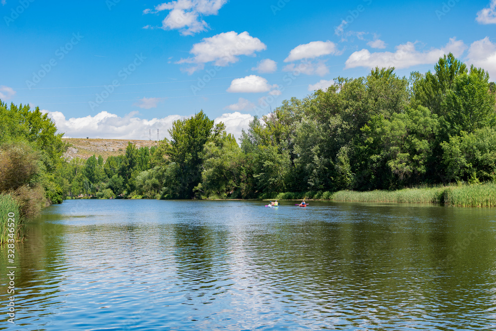The spectacular green and natural landscape under a blue sky, with a large river and a family kayaking. The spectacular green and natural landscape under a blue sky, with a large river and a family kayaking.