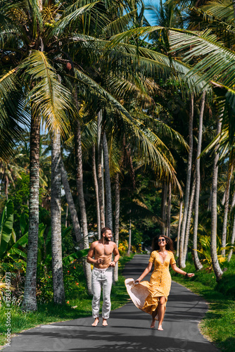 Beautiful couple running among palm trees in Bali, Indonesia. Honeymoon on the Islands. A happy couple in love runs along the road. Honeymoon trip. Wedding trip. Couple on vacation in Bali