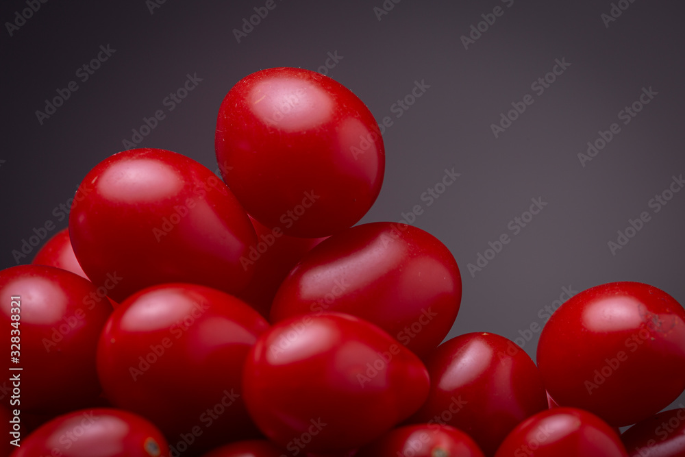 Super close up of a stack of vibrant red cherry tomatoes against a dark grey background Super close up of a stack of vibrant red cherry tomatoes against a dark grey background