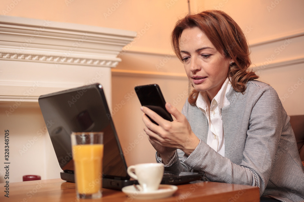 Serious mid adult Caucasian business woman typing text messages or browsing internet on a smart phone, working from a cafe Serious mid adult Caucasian business woman typing text messages or browsing internet on a smart phone, working from a cafe