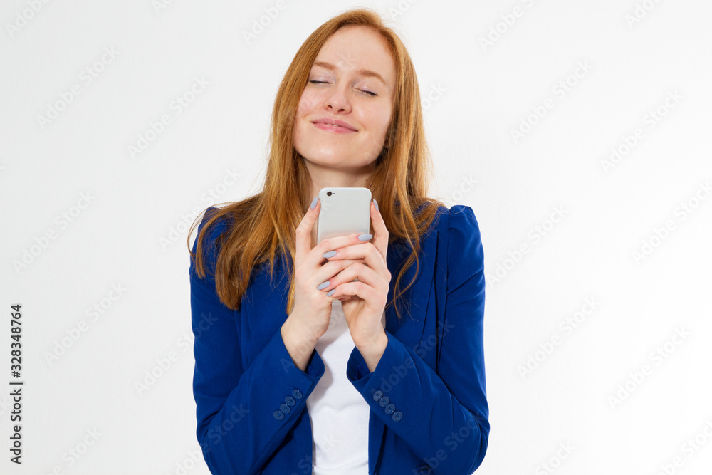 Red-hair teen lady with closed eyes holding smart phone over white Red-hair teen lady with closed eyes holding smart phone over white