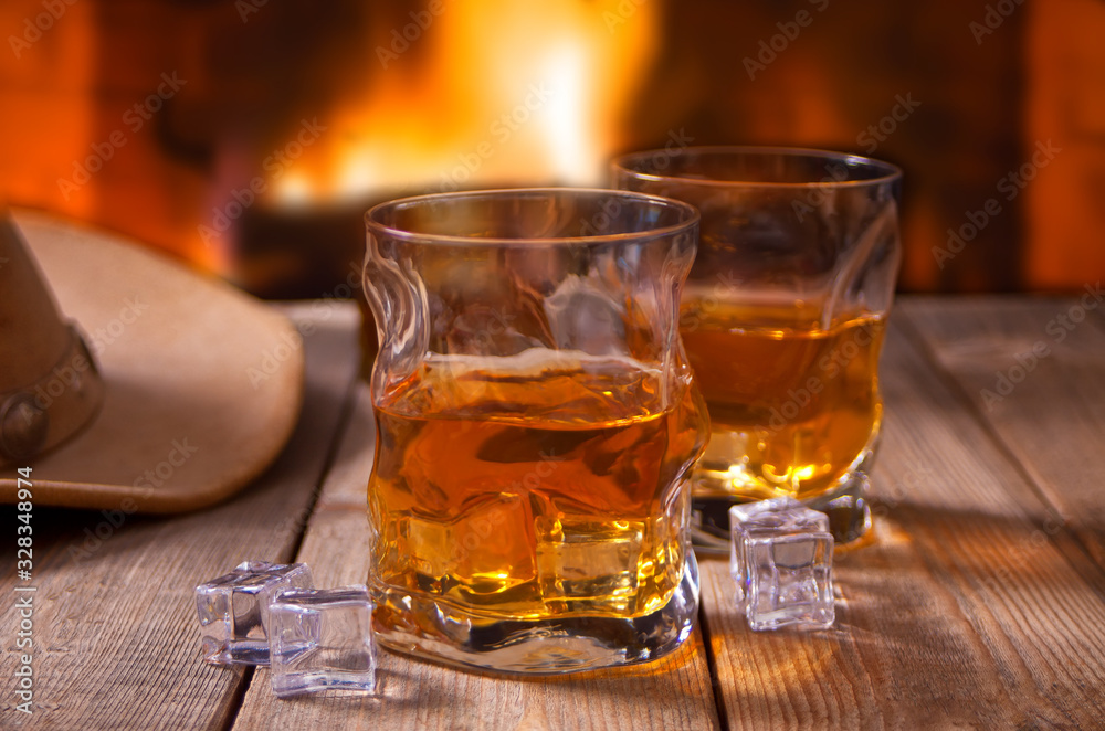 whiskey with ice on a wooden table with fireplace and cowboy hats on the background. whiskey with ice on a wooden table with fireplace and cowboy hats on the background.