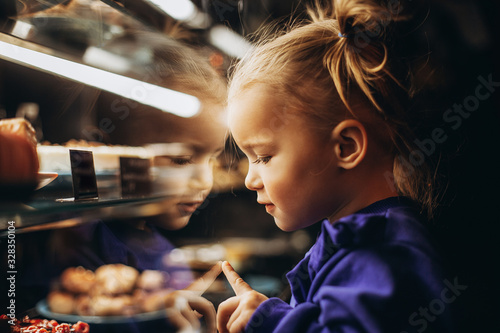 lovely girl admiringly examines a lighted showcase with various delicious cakes and desserts