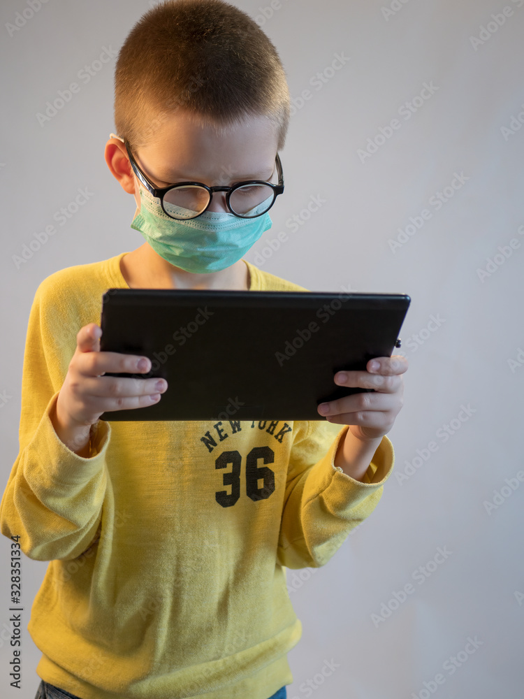 cute blonde boy in black medical mask and glasses is quarantined at home. child play with tablet and wears mask. concept of fight against the coronavirus epidemic and proper prevention of infections cute blonde boy in black medical mask and glasses is quarantined at home. child play with tablet and wears mask. concept of fight against the coronavirus epidemic and proper prevention of infections