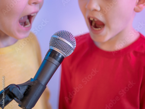 Two happy little boys received latest smartphone models as gift from their parents. children turned on music and sang karaoke in front of microphone on stand. Brothers are happy together, adore gadget