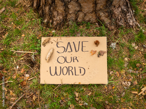 Cardboard banner with environmental message on the ground next to a tree in the forest. Save our world. Concept of sustainability © Dani