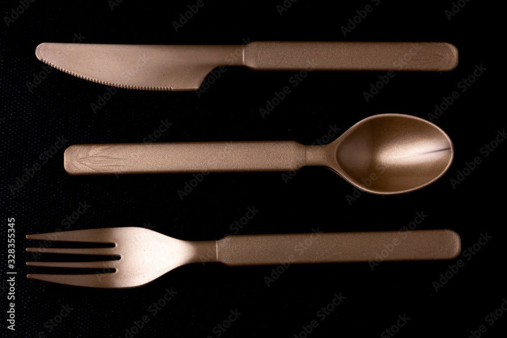 Close up of shiny dark gold coloured plastic cutlery set of horizontally ordered knife, spoon and fork laying face down Close up of shiny dark gold coloured plastic cutlery set of horizontally ordered knife, spoon and fork laying face down