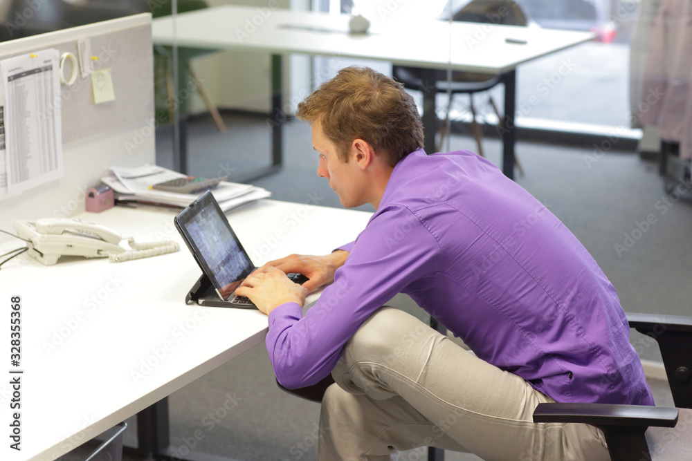 text neck - man in slouching position on office chair working with tablet at desk