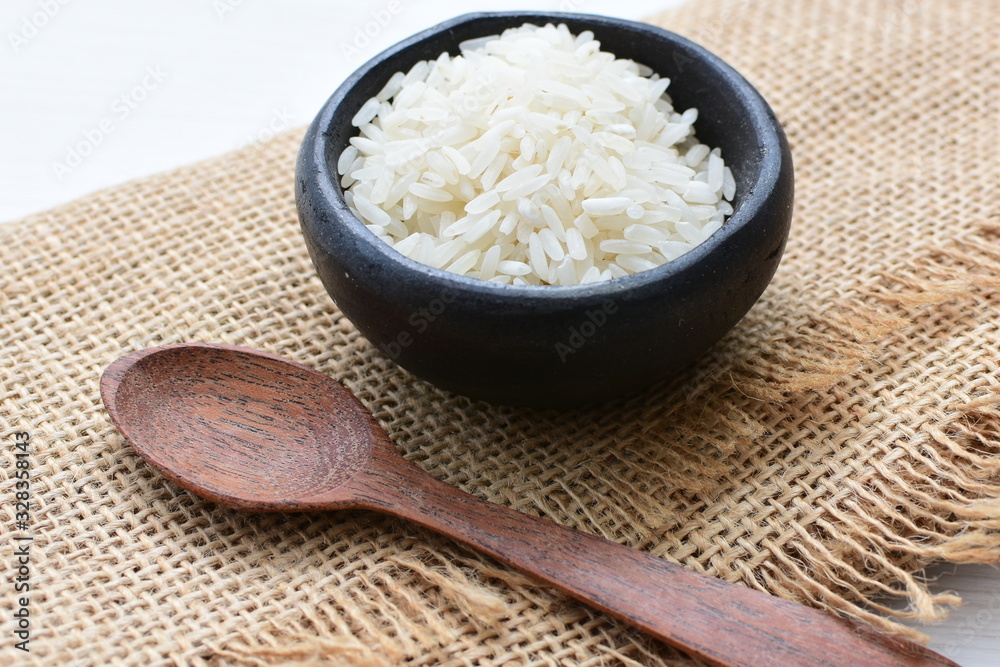 Natural raw white rice grains, on display in bowl and wooden spoon