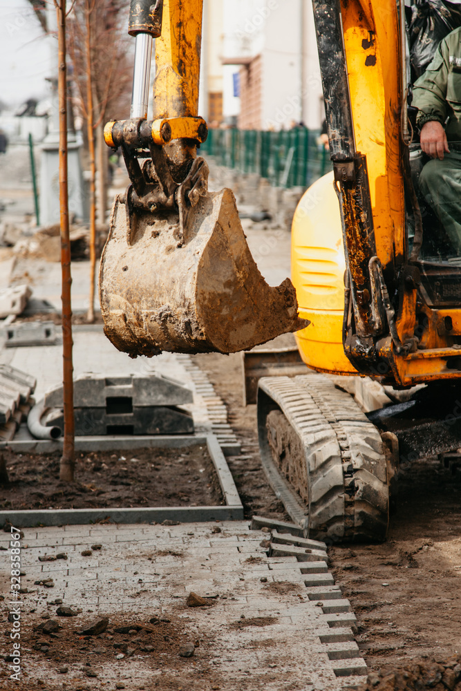 Fototapeta premium small yellow tractor with a bucket in the city