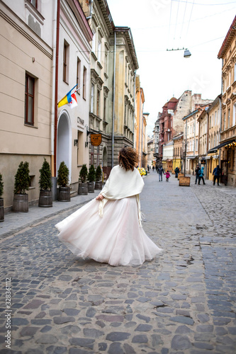 bride in a white dress walks down the street with a bouquet in her hand
