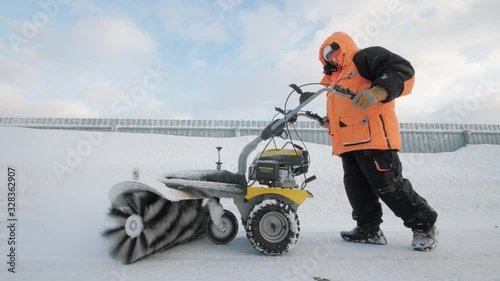 Man cleans snow in the yard with a sweeper in the winter photo