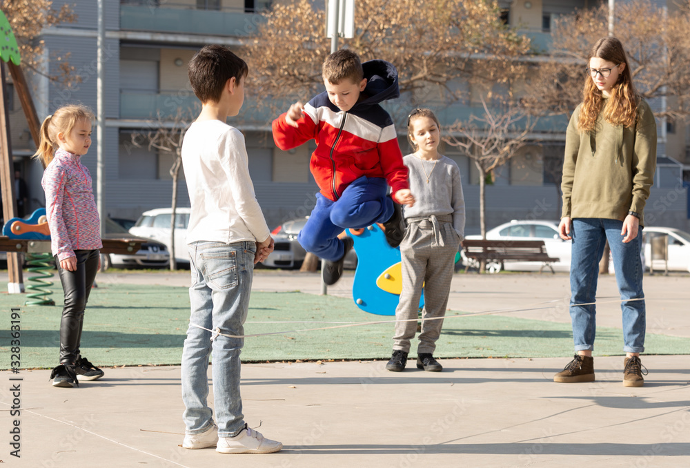 Fototapeta premium Energetic kids playing and skipping on elastic jumping rope in european yard