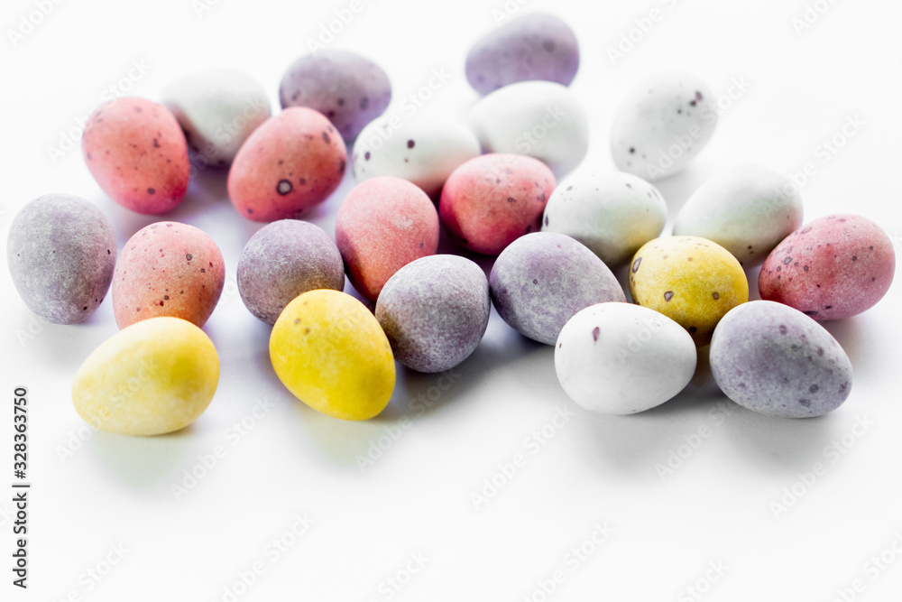 Sugar coated chocolate eggs, colorfull sweet easter treat. White background bright colours yellow, pink, violet and white eggs with dots. Copy text space, for wallpaper with easter theme. Sugar coated chocolate eggs, colorfull sweet easter treat. White background bright colours yellow, pink, violet and white eggs with dots. Copy text space, for wallpaper with easter theme.