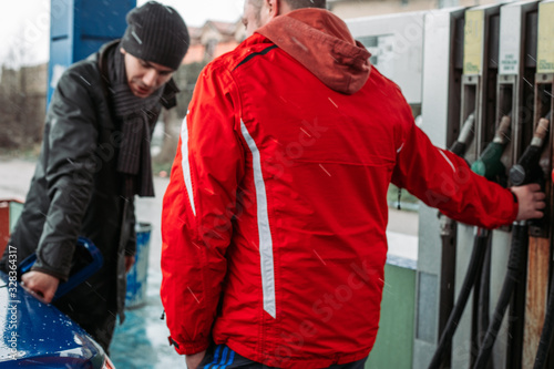 Man talking with worker at gas, petrol station. Fuel refill. Cold, rainy weather