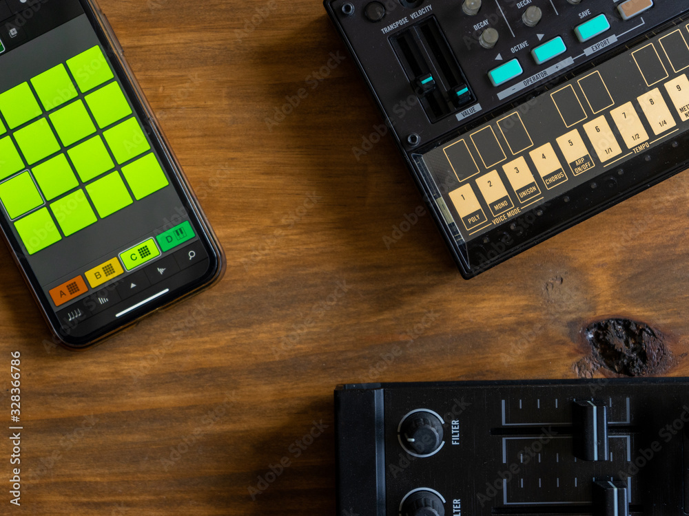Fototapeta premium Top view of fm synthesizer, midi controller and smartphone with drum machine application on a wooden table Electronic music concept
