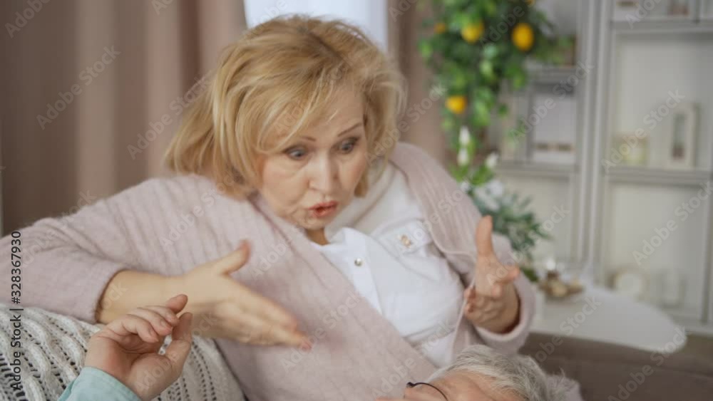 Tilt up and down shot of senior man in eyeglasses lying on lap of his wife and talking to her. Elderly woman being displeased with words of her husband and arguing with him Tilt up and down shot of senior man in eyeglasses lying on lap of his wife and talking to her. Elderly woman being displeased with words of her husband and arguing with him