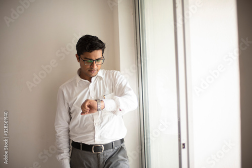 Portrait of an Indian Bengali tall, dark, handsome brunette young man in office wear is standing in front of a glass window in a corporate office/bpo/call center. Indian corporate lifestyle