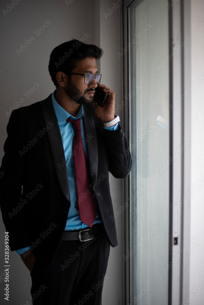 Indian Bengali tall, dark, handsome brunette young man in office wear is standing in front of a glass window showing his watch in a corporate office/bpo/call center. Indian corporate lifestyle Indian Bengali tall, dark, handsome brunette young man in office wear is standing in front of a glass window showing his watch in a corporate office/bpo/call center. Indian corporate lifestyle