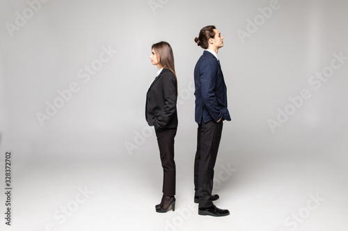 Two young business people standing back to back isolated on grey background