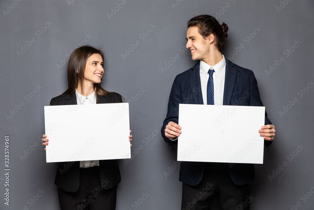 Confident business couple standing with blank board to advertise or invite isolated on gray background Confident business couple standing with blank board to advertise or invite isolated on gray background