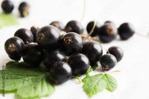 Closeup view of black currant berries with leaves on white textured background
