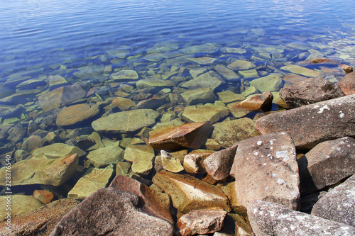 Pure clear water on the lake and large stones on the shore. Close-up. Background. Scenery.