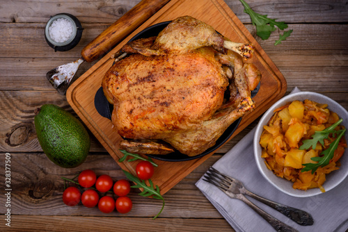 Whole roasted chicken on old wooden table with vegetables, top view