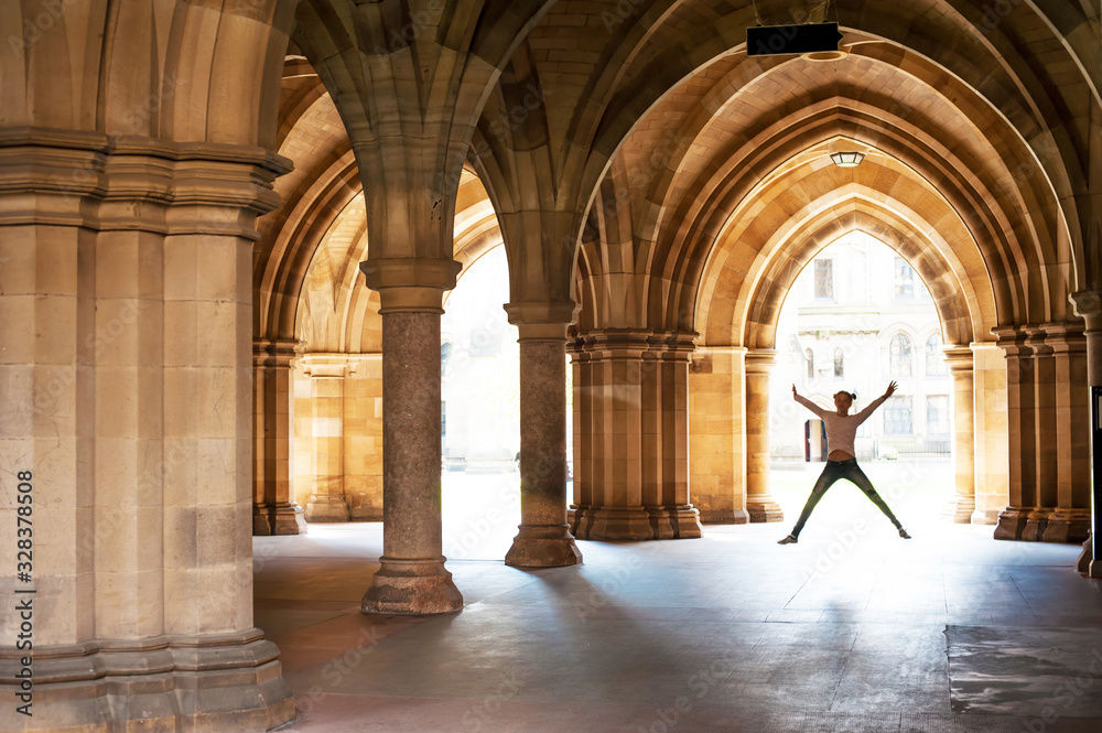  Silhouette of happy girl jumping high up in cloisters of Glasgow University