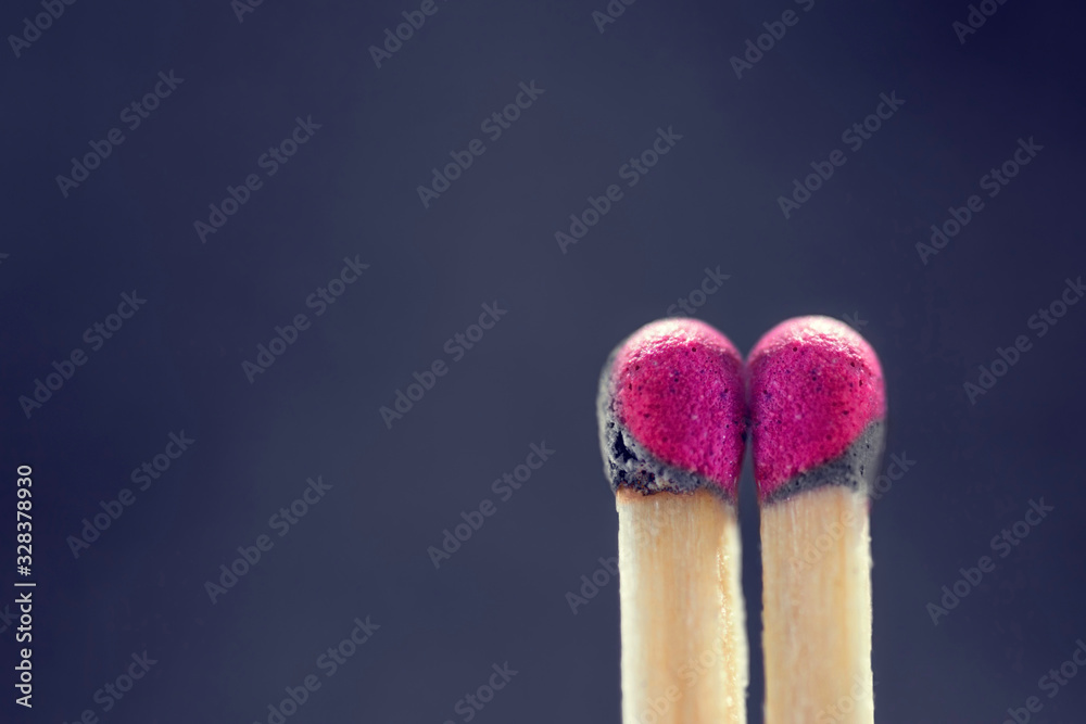 Two slightly burnt matches standing next to each other and forming a heart-shaped pattern against a violet background Two slightly burnt matches standing next to each other and forming a heart-shaped pattern against a violet background