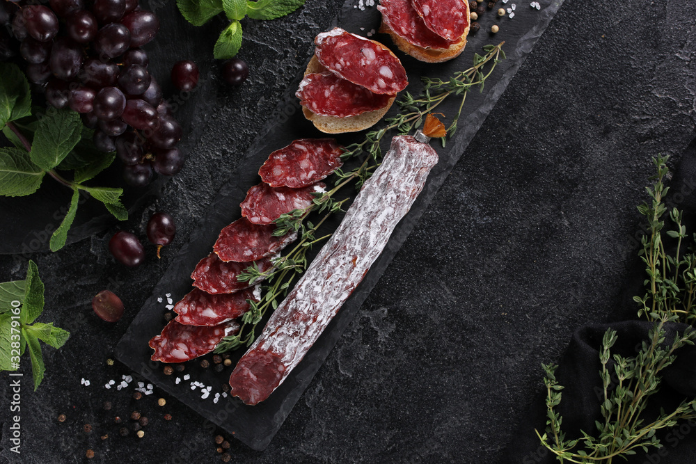 The concept of Italian cuisine. Sausage with truffle on a black board with grape, mint, thyme and spices. Background image, copy space