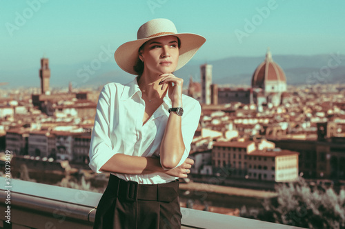 Charming stylish model in an elegant hat stands posing on Piazzale Michelangelo in Florence. View of Santa Maria Del Fiore. The concept of vacation, travel. photo