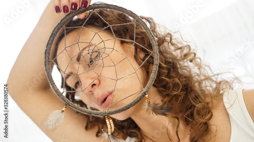 Woman with curly hair with a dream catcher in hand in front of face
