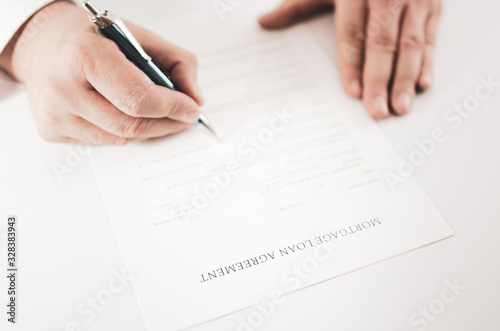 Closeup of a businessman signing a mortgage loan agreement with a pen.