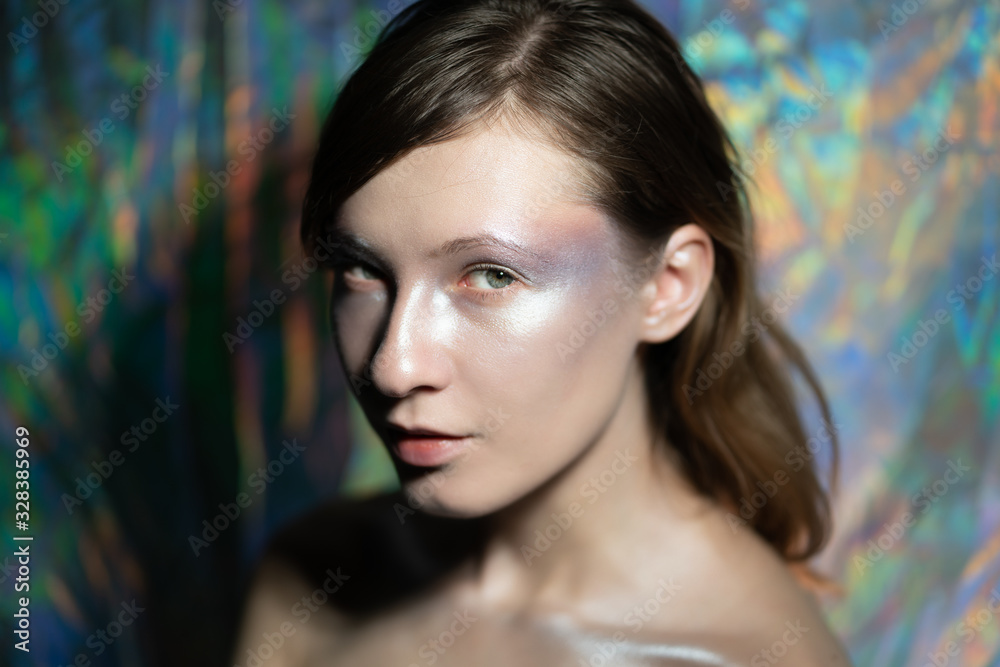 Artistic portrait of a beautiful girl with silver make-up against the background iridescent with different colors. look straight into the camera Artistic portrait of a beautiful girl with silver make-up against the background iridescent with different colors. look straight into the camera