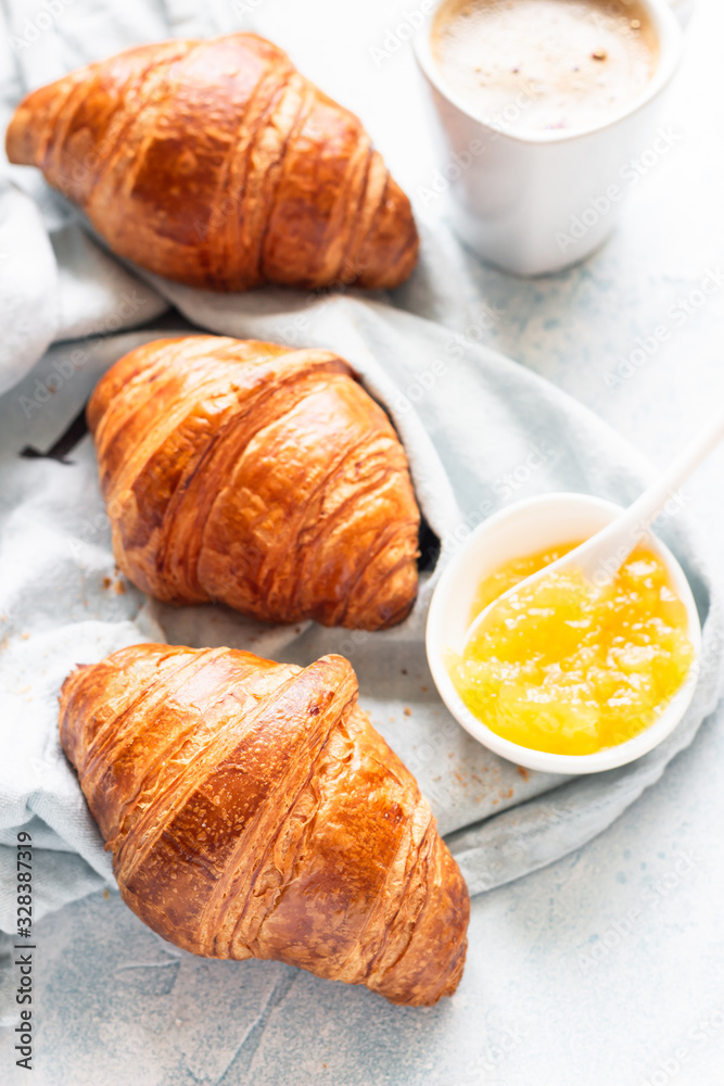 Fresh croissants on a grey linen napkin with jam and coffee. Light grey concrete background. Top view.