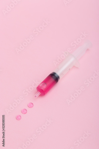 A syringe with pink liquid is half filled and lies on a pink background.