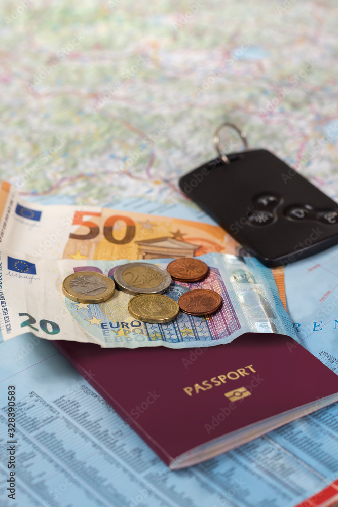 Banknoty i monety Euro leżą na mapie samochodowej. Paszport i kluczyki samochodowe również leżą na papierowej mapie.