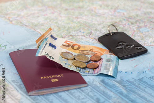Papierowa mapa samochodowa na której leży paszport banknoty i monety euro oraz karta do samochodu.