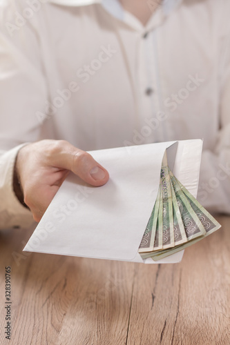 Obraz na płótnie Męska dłoń trzyma białą kopertę wypełnioną banknotami polskiej waluty i podaje ją ponad stołem. w salonie