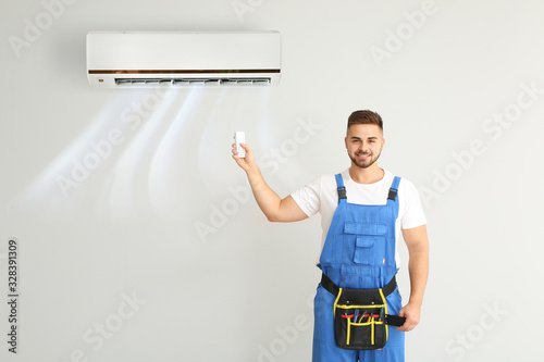 Male technician switching on air conditioner on light wall