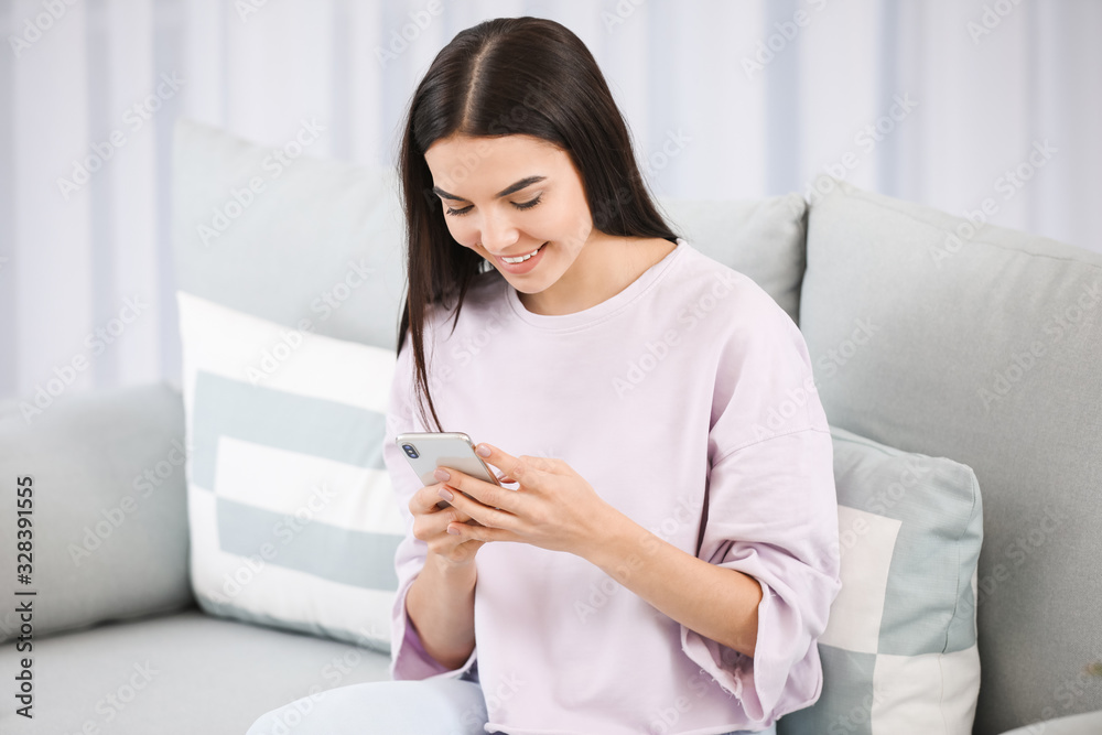 Young woman with mobile phone sitting on sofa at home Young woman with mobile phone sitting on sofa at home
