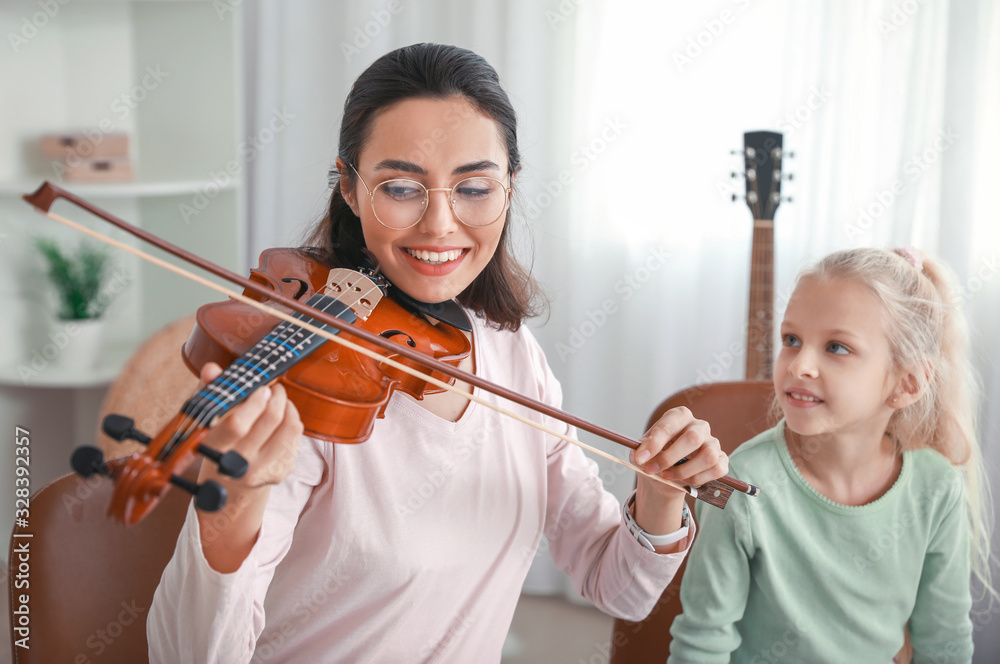 Private music teacher giving violin lessons to little girl at home
