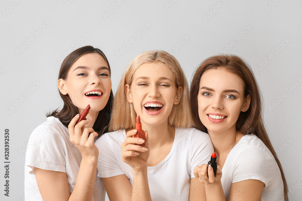 Beautiful young women applying makeup on light background Beautiful young women applying makeup on light background