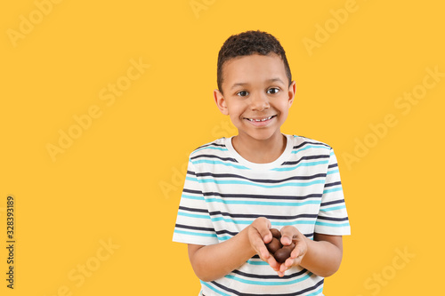 Cute African-American boy with sweet chocolate eggs on color background