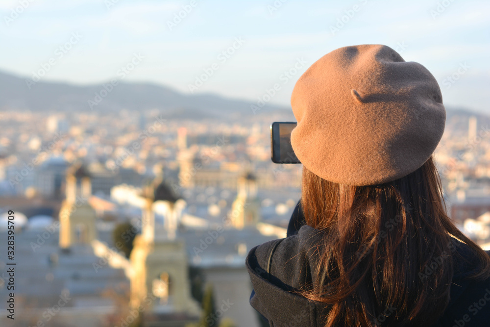 Fototapeta premium Fashion tourist girl with a hat on her back taking pictures with her smartphone to a city.Barcelona. Concept: tourism, travel, vacations