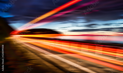 Long exposure capturing red and orange light trails from a speeding truck at the coast