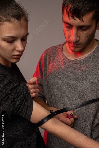 Young sloppy couple, man holding drug syringe injection heroin to her girlfriend's hand. Social disaster and epidemic of narcotic addiction concept