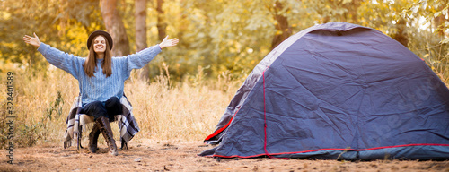 Banner format photo of camping holiday, tourist traveler woman with hands up in sweater and black hat ralaxing in camp tent in forest, rest vacation concept photo