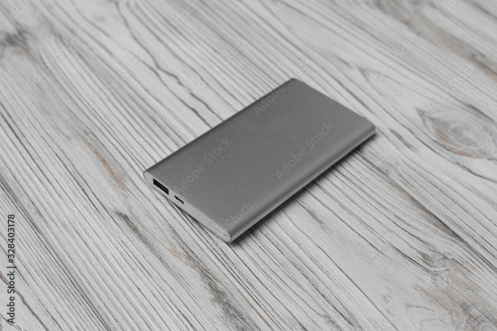 silver powerbank with usb on wooden background close up. portable charger for mobile phones and other gadgets without electrical outlet isolated on gray background. silver powerbank with usb on wooden background close up. portable charger for mobile phones and other gadgets without electrical outlet isolated on gray background.